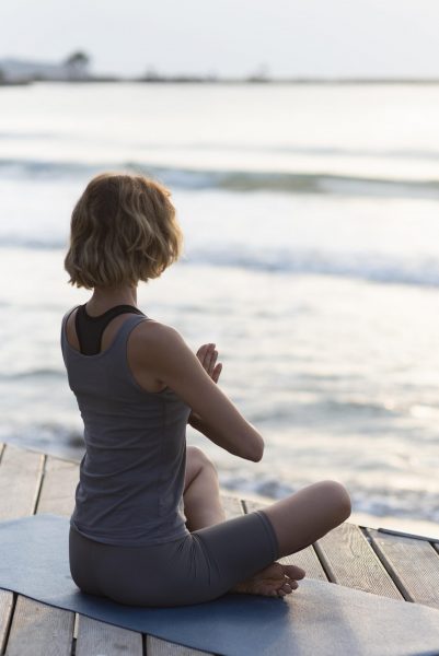 full-shot-woman-doing-sukhasana-mat-facing-sea